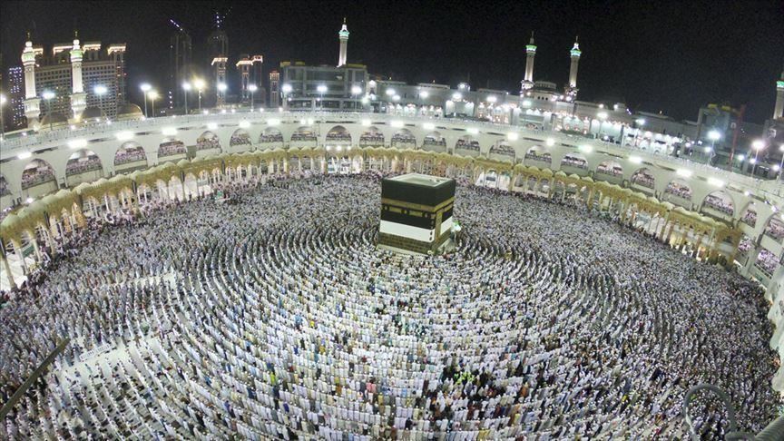 حجاج واقفون على جبل عرفات تحت الشمس، بينما يرفرف علم المملكة العربية السعودية في الأفق، في خلفية روحانية عظيمة.